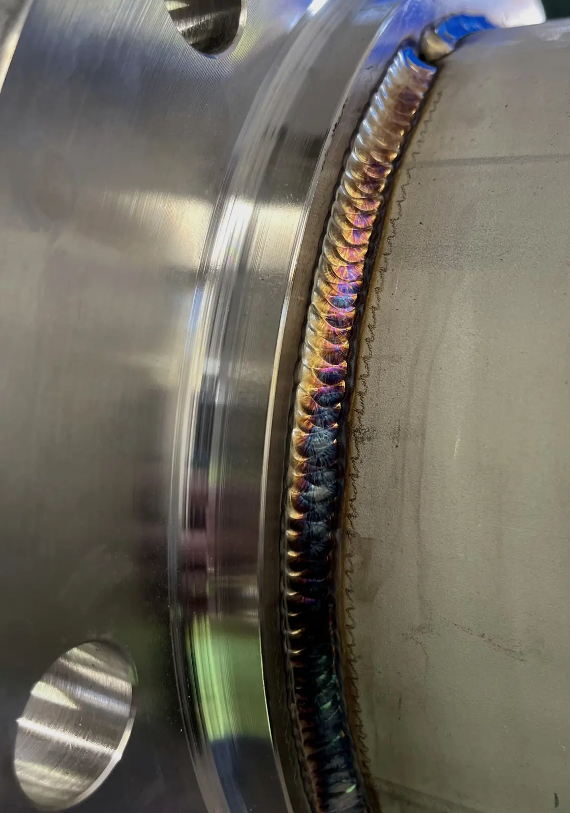 Stainless flange-to-pipe TIG weld with heat tint colors along the bead